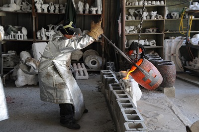 Wearing a fireproof suit, a foundry worker pours molten bronze into a Rosa Parks mold. Credit: Scott Polanca.