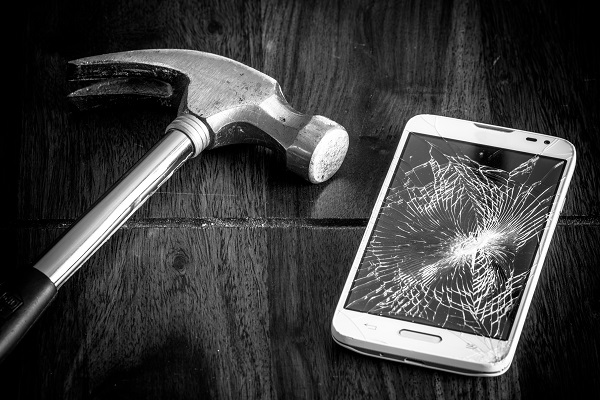 A hammer rests next to a cracked phone screen.